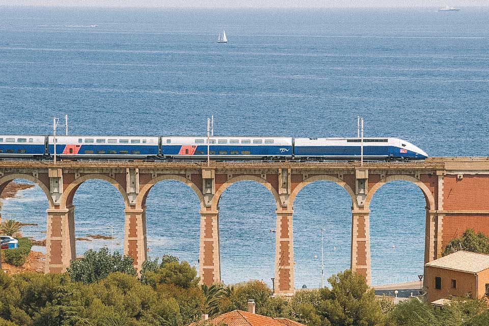 Trem TGV passando por ferrovia suspensa com o mar ao fundo