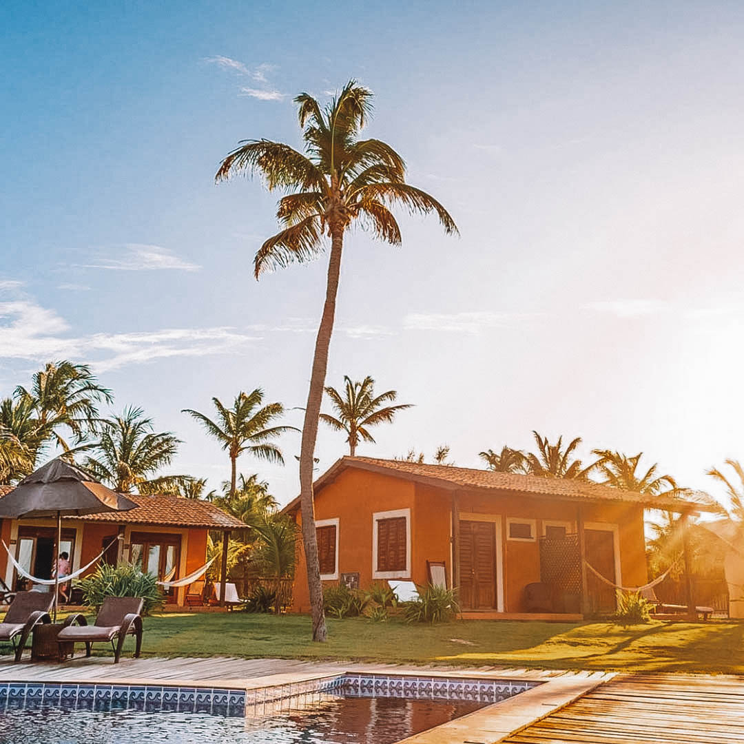 Pôr do sol com uma casinha laranja no gramado e uma grande palmeira ao lado