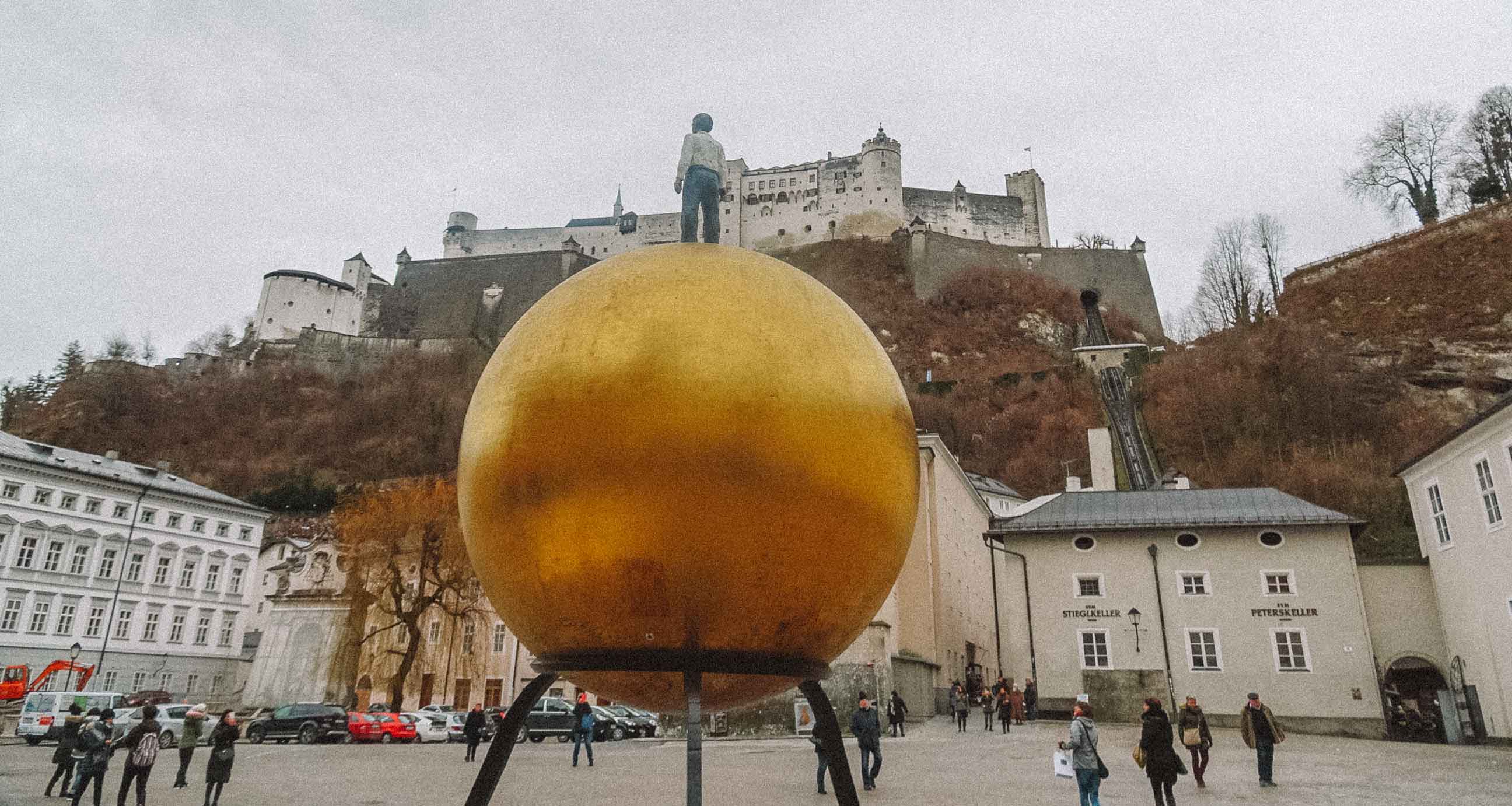Estátua de uma esfera dourada com um homem em cima em uma praça de Salzburgo