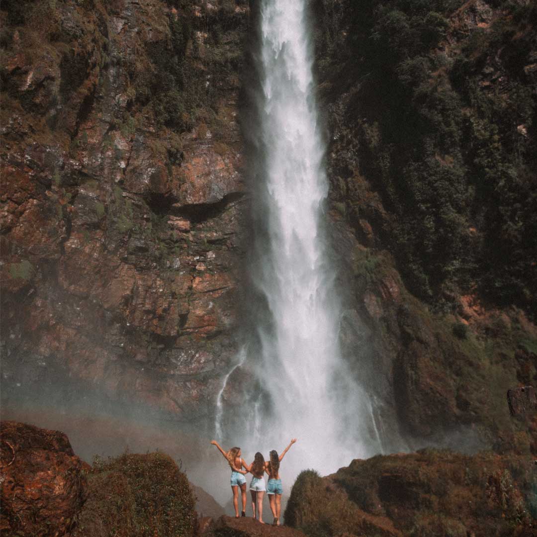 Três mulheres em pé na base da cachoeira do Itiquira