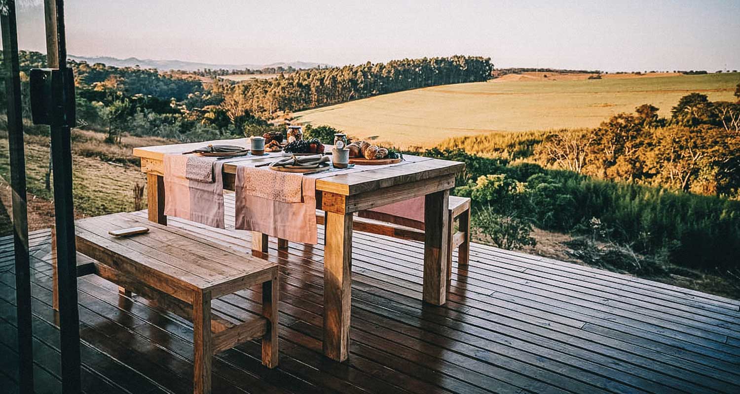 Deck de madeira com mesa e bancos com café da manhã servido