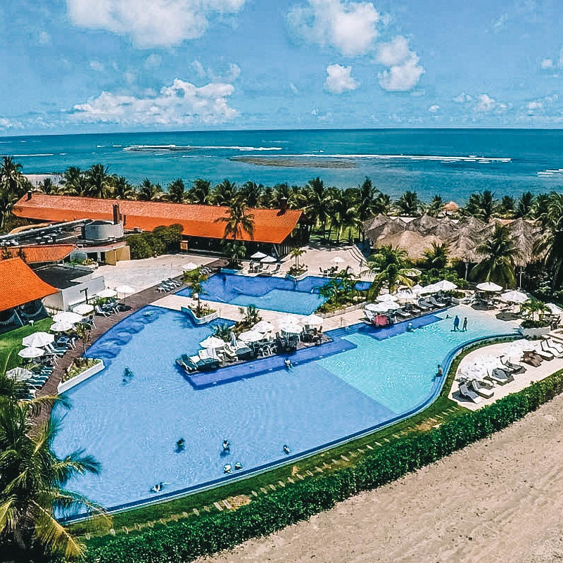 Vista aérea de todo o complexo do resort, abrangendo as acomodações, piscina, jardim e a vista beira-mar