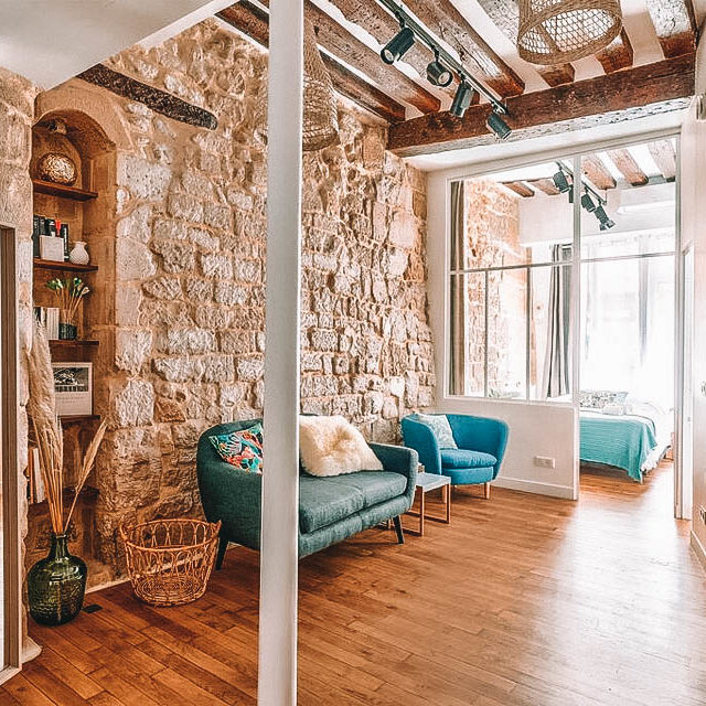 Apartamento com vigas e chão em madeira, parede de pedra e sofá azul esmeralda